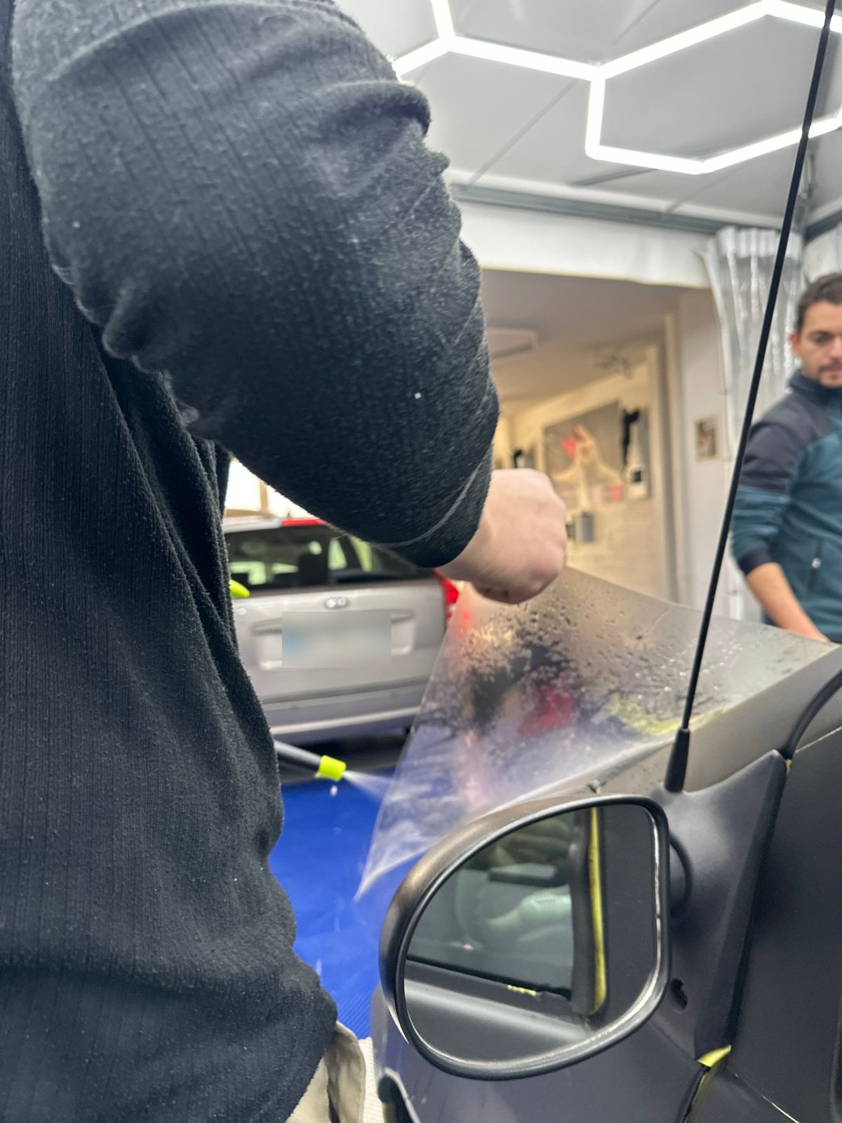 Un poseur applique un film transparent sur un rétroviseur dans un atelier