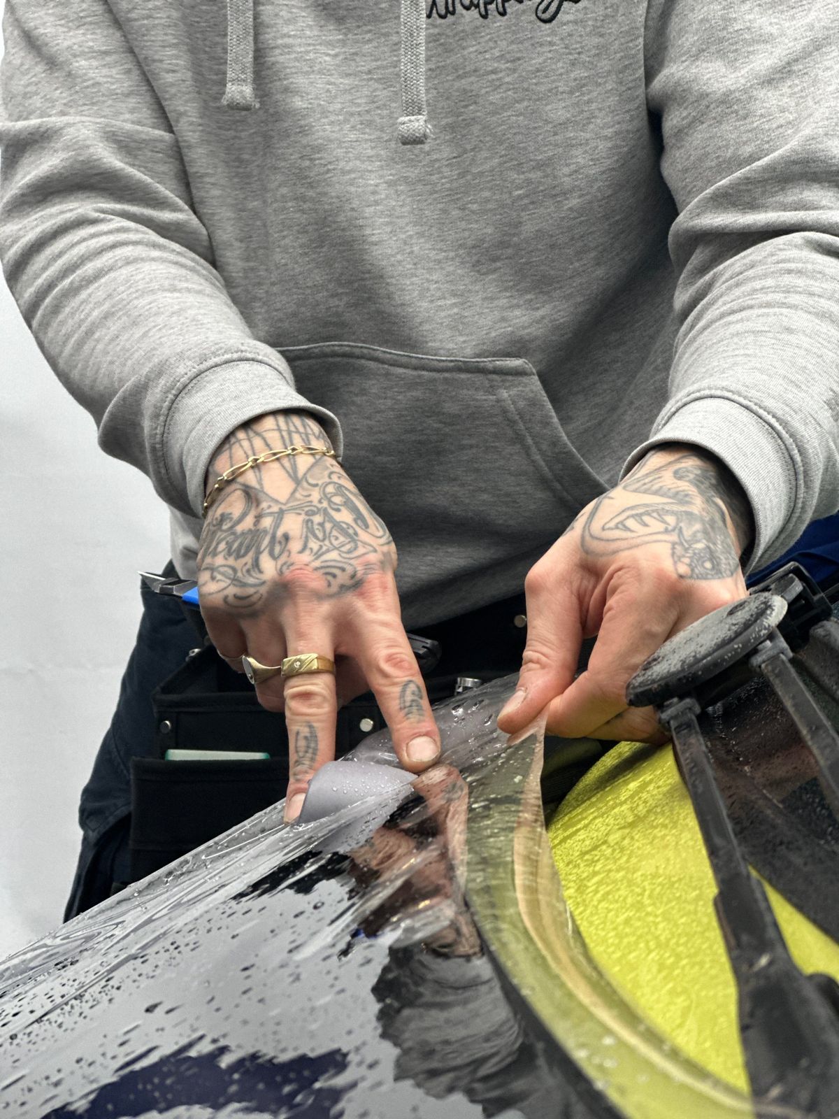 Mains tatouées lissant un film sur un capot noir