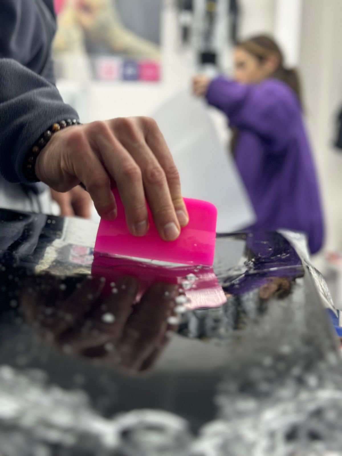 Raclette rose passée sur un film humide, capot noir brillant